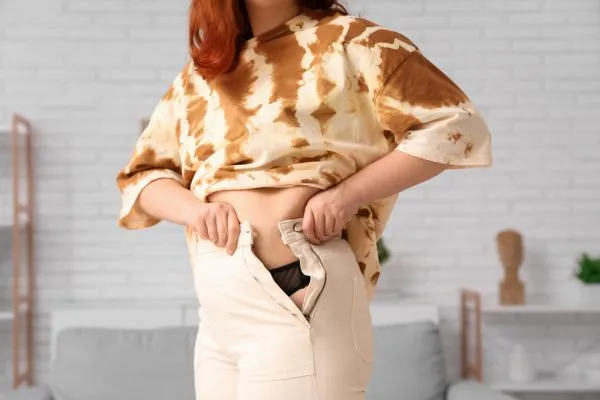 Image of woman trying to do her trousers up after pregnancy weight gain Newton Mearns