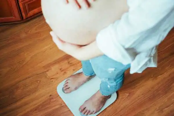 Image of woman weighing herself and experiencing weight gain through pregnancy Newton Mearns